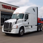 White semi truck with aerodynamic cab parked in front of a commercial truck dealership, ideal for business use